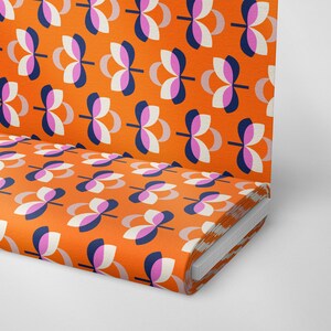 K&ouml;nnte beinhalten: Orangener Stoff mit einem sich wiederholenden Muster aus stilisierten Blumenformen in Wei&szlig;, Marineblau und Rosa. Der Stoff ist aufgerollt und zeigt das Muster auf der Oberseite und der Seite. Das Design ist im Retro-Stil der Moderne der Mitte des Jahrhunderts.