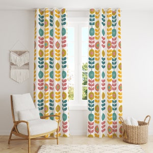 May include: A pair of white curtains featuring a repeating floral pattern in teal, yellow, pink, and olive green. The curtains are hanging in front of a window. A chair and basket are visible in the room.