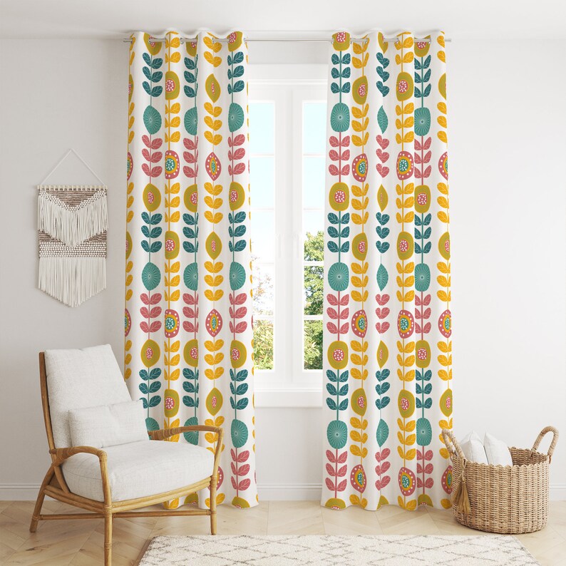 May include: A pair of white curtains featuring a repeating floral pattern in teal, yellow, pink, and olive green. The curtains are hanging in front of a window. A chair and basket are visible in the room.
