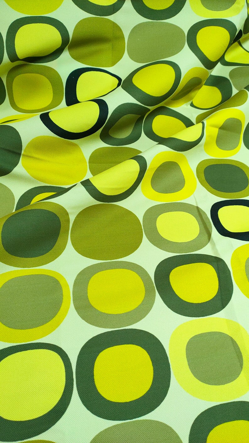 May include: A fabric with a repeating pattern of green and yellow circles. The circles are of varying sizes and are arranged in a random pattern.