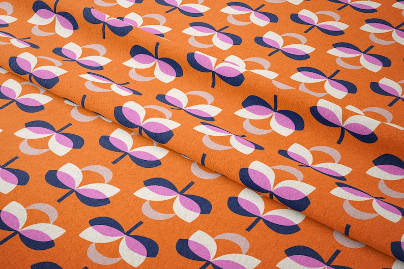 K&ouml;nnte beinhalten: Nahaufnahme eines orangefarbenen Stoffes mit einem sich wiederholenden Blumenmuster. Die Blumen bestehen aus wei&szlig;en, rosa und marineblauen Bl&uuml;tenbl&auml;ttern mit einem hellgrauen, gebogenen Akzent. Der Stoff hat ein strukturiertes Aussehen.