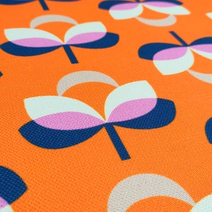 K&ouml;nnte beinhalten: Nahaufnahme eines Stoffes mit einem sich wiederholenden Blumenmuster. Die Blumen haben wei&szlig;e, rosa und beige Bl&uuml;tenbl&auml;tter mit marineblauen und schwarzen Stielen und Akzenten, vor einem leuchtend orangefarbenen Hintergrund. Der Stoff hat ein strukturiertes Aussehen.