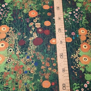May include: A fabric featuring a dense floral pattern with orange, red, and yellow flowers on a dark green background. A wooden ruler is placed vertically on the right side, showing measurements from 20 to 65 inches for scale reference.