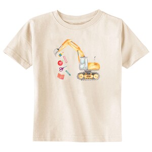 Puede incluir: Camiseta color crema con una ilustraci&oacute;n en acuarela de una excavadora amarilla. El brazo de la excavadora est&aacute; levantado, derramando &uacute;tiles escolares como una manzana roja, tijeras y l&aacute;pices. El dise&ntilde;o est&aacute; centrado en la parte delantera de la camiseta.