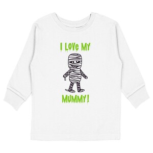 May include: A white long-sleeve shirt featuring a black and white line drawing of a wrapped mummy character in the center. Above and below the mummy, the text reads I LOVE MY MUMMY! in a bright green, dripping-style font on the front.