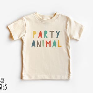 May include: A cream-colored short-sleeve t-shirt featuring the text PARTY ANIMAL printed in a multi-colored, sans-serif font. The letters are colored in yellow, red, teal, brown, and blue, arranged in two lines across the center of the chest.
