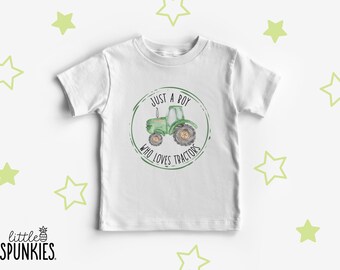 May include: A white short-sleeved t-shirt featuring a circular graphic with a green watercolor tractor in the center. The text surrounding the tractor reads, "JUST A BOY WHO LOVES TRACTORS" in black lettering. The shirt is surrounded by light green stars.