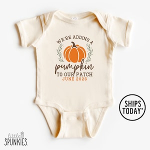 May include: Cream-colored baby bodysuit with the text "WE'RE ADDING A pumpkin TO OUR PATCH JUNE 2026" in brown and orange. The design includes an orange pumpkin and green leaves. The bodysuit has short sleeves.