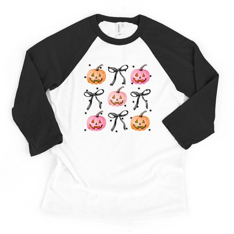 May include: A white baseball-style t-shirt with black three-quarter length sleeves featuring a repeating pattern of orange and pink jack-o'-lantern pumpkins, black bows, and small black stars printed on the front center of the garment.