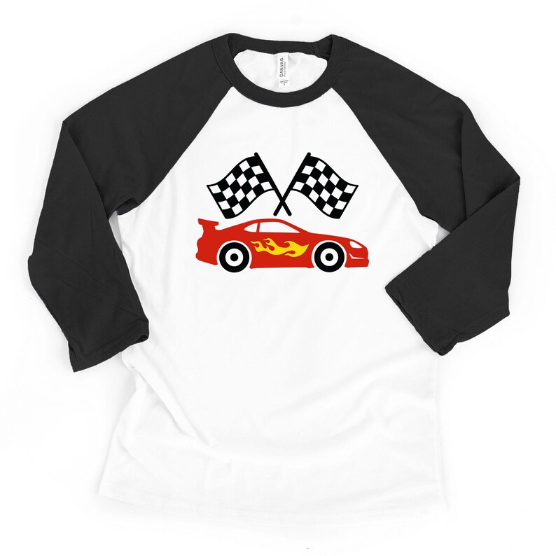 May include: A white baseball t-shirt with black three-quarter length sleeves featuring a graphic of a red sports car with yellow flames on the side, positioned below two crossed black and white checkered racing flags on the chest area.
