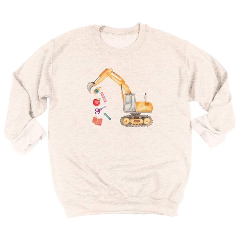 Puede incluir: Sudadera gris claro con una ilustraci&oacute;n en acuarela de una excavadora amarilla con un cuchar&oacute;n negro. La excavadora levanta &uacute;tiles escolares, incluyendo una manzana roja, tijeras y un libro. La sudadera tiene cuello redondo y mangas largas.