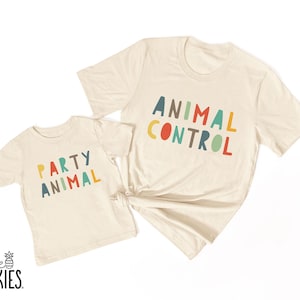 May include: Two cream-colored short-sleeve t-shirts. The smaller shirt features the text "PARTY ANIMAL" in multicolored letters. The larger shirt features the text "ANIMAL CONTROL" in multicolored letters. The text "little SPUNKIES" is in the corner.