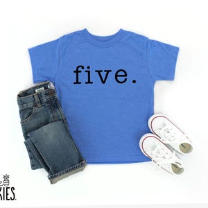 May include: A bright blue short-sleeved t-shirt with the word five. printed in black lowercase letters across the chest, paired with dark blue denim jeans and a pair of white low-top canvas sneakers with white laces and rubber soles.