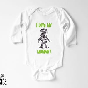 May include: A white long-sleeve baby bodysuit featuring a black line-art illustration of a mummy character centered on the chest. Above and below the mummy, the text reads I LOVE MY MUMMY! in a bright green, dripping-style font.