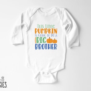 May include: A white long-sleeve baby bodysuit featuring the text "This Little PUMPKIN IS GOING TO BE A BIG BROTHER" in green, orange, and blue, accompanied by two orange pumpkin illustrations. The brand logo "little SPUNKIES" is in the corner.