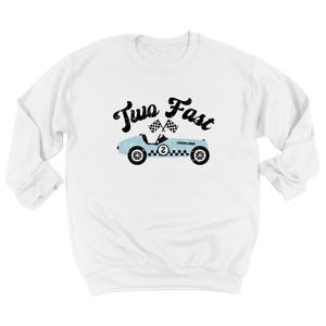 May include: A white long-sleeve sweatshirt featuring a graphic of a light blue vintage race car with the number two on the side, two checkered flags above it, and the black text Two Fast written in a distressed font style across the chest.