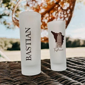 Könnte beinhalten: Zwei gefrostete Schnapsgläser aus Glas. Ein Glas hat den Schriftzug "BASTIAN" aufgedruckt. Das andere Glas hat einen braunen Umriss der Region Toskana, Italien, mit dem Schiefen Turm von Pisa im Umriss. Der Text "Toscana" ist unter dem Umriss aufgedruckt.