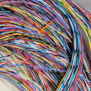 May include: A bundle of colorful electrical wires, including red, yellow, blue, green, and purple, are held together with an orange cable tie. The wires are tightly packed together, creating a vibrant and intricate pattern.