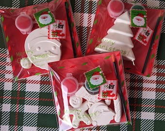 Puede incluir: Tres kits de pintura de cerámica con temática navideña con pintura roja y blanca, pinceles y adornos de cerámica blanca. Los adornos incluyen un muñeco de nieve, un árbol de Navidad y un Papá Noel.