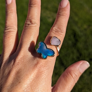 May include: A gold ring with a blue butterfly and a pink heart shaped stone. The ring is adjustable and can be worn on any finger.
