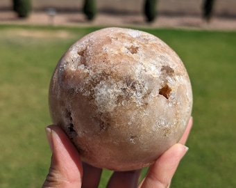 Puede incluir: Una gran geoda redonda de color marrón claro con una superficie rugosa y texturizada. La geoda tiene una gran abertura que revela un interior cristalino blanco.