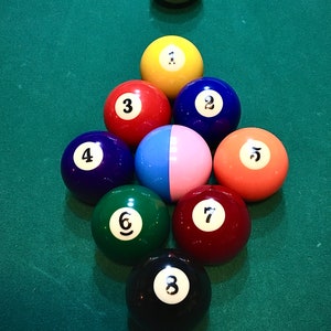 May include: A set of billiard balls arranged in a triangle formation on a green felt pool table. The balls are numbered 1 through 8, with a white cue ball at the top of the triangle.
