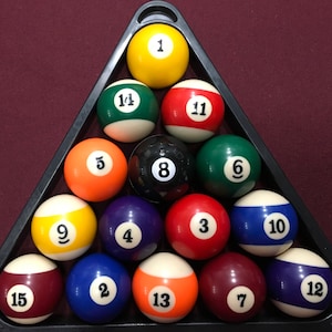 May include: A triangle rack of billiard balls, with numbers 1 through 15, including the 8 ball in the center. The balls are arranged in a pyramid shape, with the 1 ball at the top and the 15 ball at the bottom.