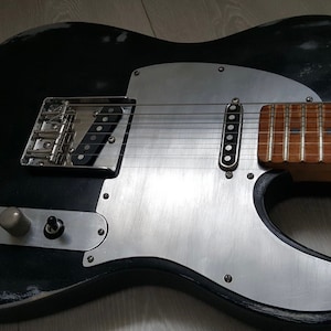 May include: A black electric guitar with a silver pickguard and a wooden fretboard. The guitar has a worn, distressed look.