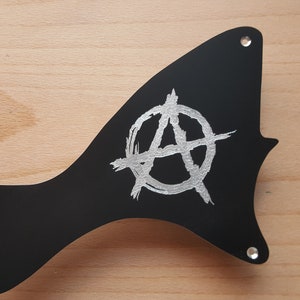May include: Black guitar pickguard with a silver anarchy symbol.