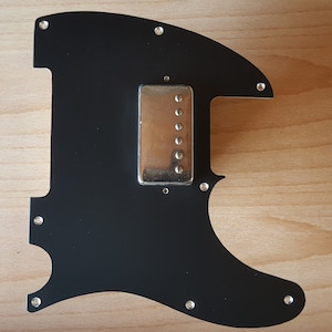 May include: Black guitar pickguard with a silver humbucker pickup and multiple screw holes.