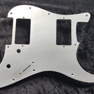 May include: A silver metal guitar pickguard with two pickup cutouts and a control plate cutout.