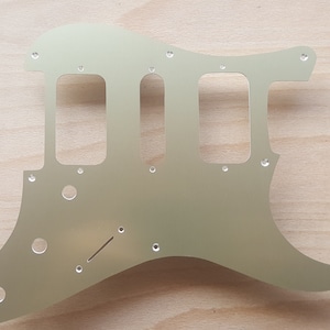 May include: A plain, silver-colored metal guitar pickguard with multiple holes and cutouts for mounting and electronics.