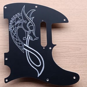 May include: Black guitar pickguard with a silver dragon design. The dragon is in a Celtic knot style.