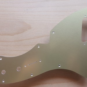 May include: A gold-colored metal guitar pickguard with multiple screw holes and a cutout for a pickup.