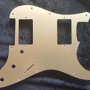 May include: A gold-colored metal guitar pickguard with two rectangular cutouts for pickups and several small holes for screws.