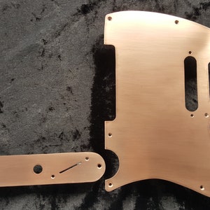 May include: A set of two copper-colored guitar pickguards. The larger pickguard is shaped like a guitar body, while the smaller pickguard is rectangular. Both pickguards have cutouts for knobs and other guitar hardware.