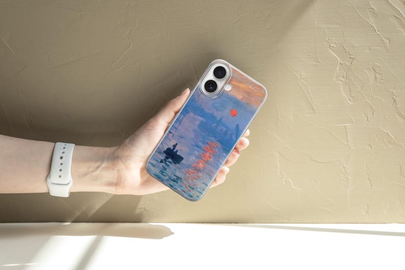 May include: A clear smartphone case featuring a printed reproduction of an impressionist painting depicting a harbor scene at sunrise with a small boat, blue water, and a bright orange sun reflecting on the surface, with two camera lens cutouts.
