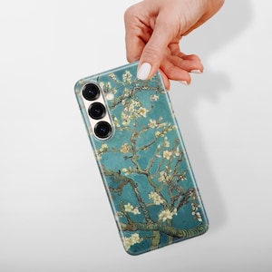 May include: A rectangular smartphone case featuring a teal blue background with a detailed print of brown tree branches and white almond blossoms. The case has three circular camera lens cutouts arranged vertically on the upper left side.