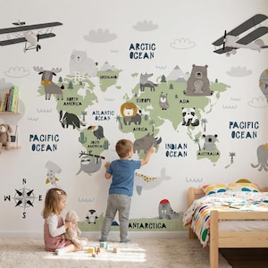 May include: A whimsical world map wall decal featuring continents in green with animal illustrations and ocean names in navy blue. Two children interact with the map, with airplanes and a hot air balloon adding to the playful design. A wooden bed and bookshelf are also visible.