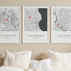May include: Three framed wall art prints featuring black and white city street maps with a single red heart icon on each. The prints are labeled OUR FIRST DATE, OUR WEDDING, and OUR HOME, with specific dates and city names printed below each map.