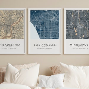 May include: Three framed city maps with white frames and a beige background. The maps are of Philadelphia, Los Angeles, and Minneapolis. The maps are in a blue and beige color scheme.