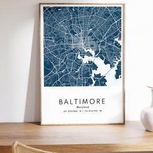 May include: A framed map of Baltimore, Maryland, in a dark blue color scheme. The map shows the city's streets and waterways. The text below the map reads "Baltimore, Maryland, 39.290386&deg; N / 76.612190&deg; W".