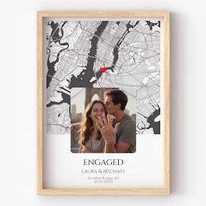May include: Framed print featuring a black and white map of New York City with a red heart marking a location. A photo of a couple is below the map, with the word "ENGAGED" and names and a date printed below the photo.