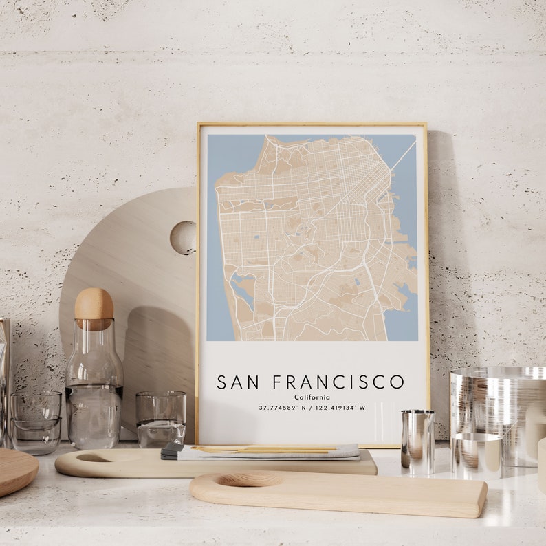 May include: A framed map of San Francisco, California with a light blue background and beige lines showing the streets. The text "SAN FRANCISCO" and "California" is printed below the map, along with the coordinates "37.774889&deg; N / 122.419134&deg; W".