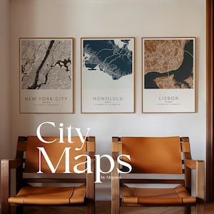 May include: Three framed city maps of New York City, Honolulu, and Lisbon, each with a unique color scheme. The maps are displayed above two wooden chairs with tan leather seats. The text "City Maps" is displayed in large white letters.