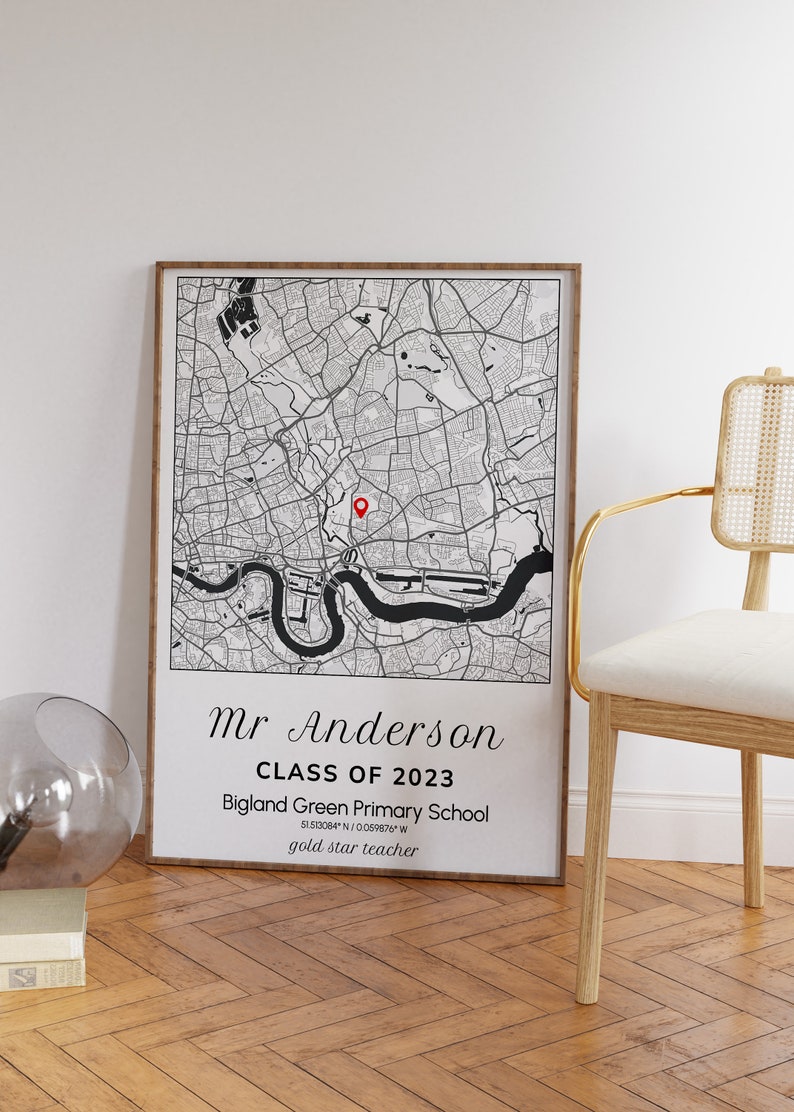 May include: A framed black and white map print featuring a detailed city map with a red marker. The print includes the text "Mr Anderson CLASS OF 2023 Bigland Green Primary School gold star teacher". The frame is a light brown color.