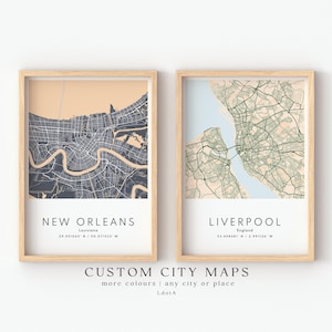 May include: Two framed city maps, one of New Orleans and one of Liverpool, with a light wood frame. The New Orleans map is in shades of gray and the Liverpool map is in shades of green. The text "CUSTOM CITY MAPS" is at the bottom.