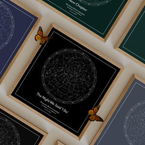 May include: A collection of framed star map prints. Each print features a black background with a white constellation design. The prints are in wooden frames with white borders. Text on the prints reads "The Night We Said 'I Do'" and "New Chapter". Orange butterflies decorate the frames.