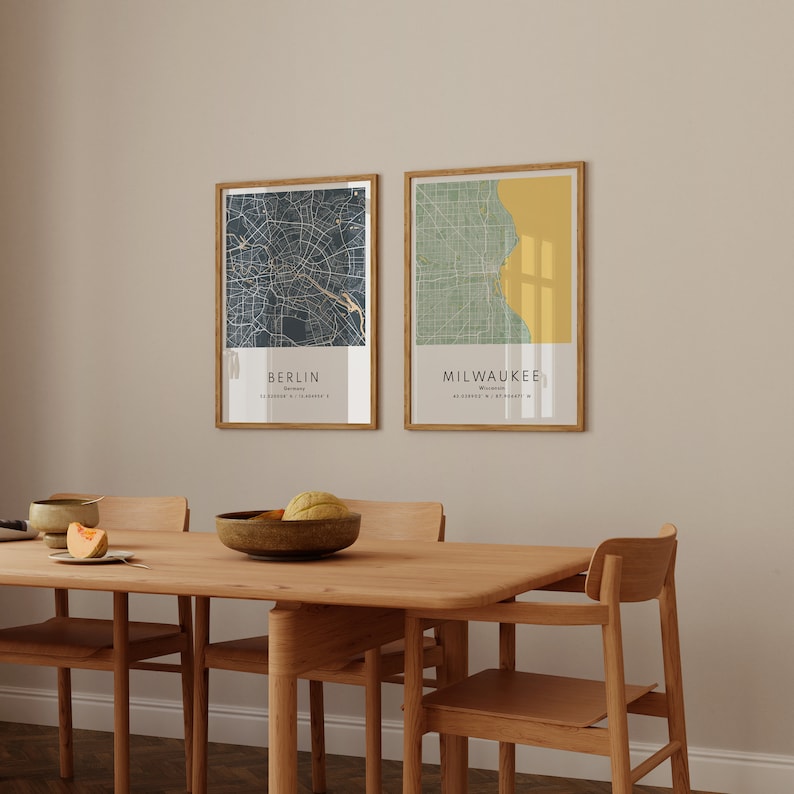 May include: Two framed city maps, one of Berlin, Germany and one of Milwaukee, Wisconsin, hanging on a beige wall above a wooden dining table with four chairs.