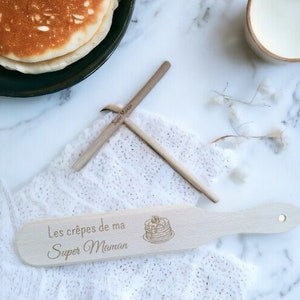 May include: A wooden spatula with the text "Les crêpes de ma Super Maman" and a drawing of a stack of pancakes.